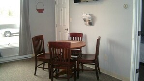 A dining area with a table and four chairs, a door, a window with curtains, a wall-mounted TV, and a bulletin board. - Killington / Rutland 1 Bdroom Cabin, Cabin #1 (Mendon)