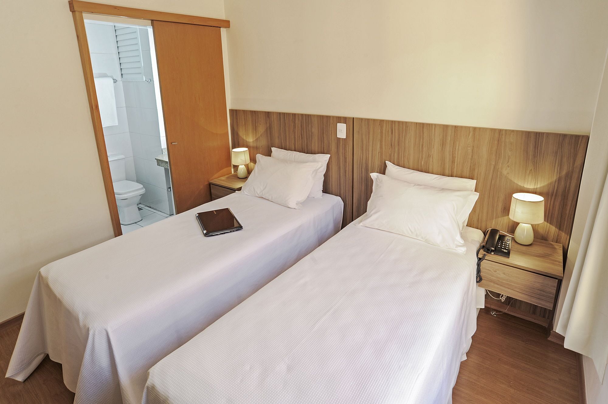 Ein Hotelzimmer mit zwei Einzelbetten, einem Nachttisch mit Lampe, einem Nachttischtelefon und einem durchgehenden Türspalt erkennbaren Badezimmer.
