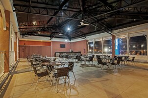 A spacious indoor dining area with high ceilings and large windows, featuring multiple tables and chairs.