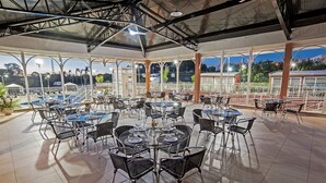 A spacious outdoor dining area with multiple tables and chairs, large windows offering views of the cityscape, and a covered roof structure. - The Hill Executive (São Carlos)