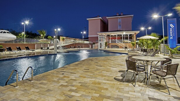 A pool area with lounge chairs and a building with a sign reading "Slaviero Executive". - The Hill Executive (São Carlos)