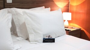 A hotel room with a neatly made bed, a nightstand with a lamp, and a small sign on the bed. - The Hill Executive (São Carlos)