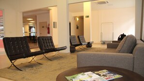 A modern living room with a sofa, two black leather chairs, a coffee table with magazines, and a carpeted floor. - The Hill Executive (São Carlos)
