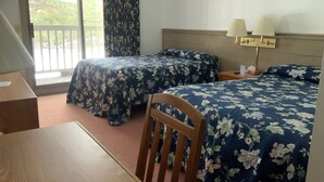 Habitación de hotel con dos camas, una silla de madera, un escritorio y un balcón con cortinas.