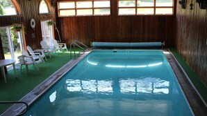 Una piscina interior con una pared de madera, suelo verde y sillas blancas alrededor.