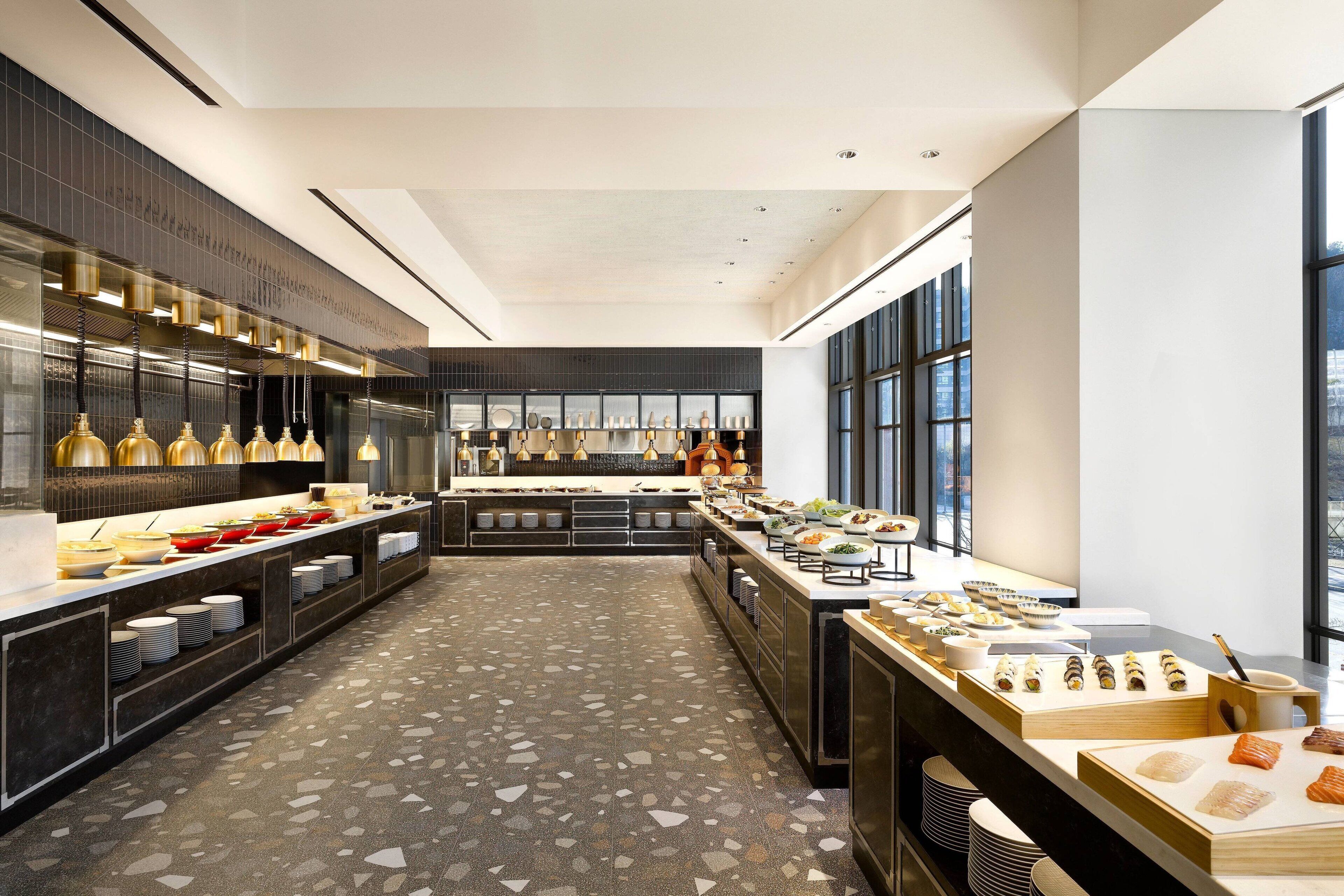 A modern hotel kitchen with a long counter displaying various food items and a tiled floor.