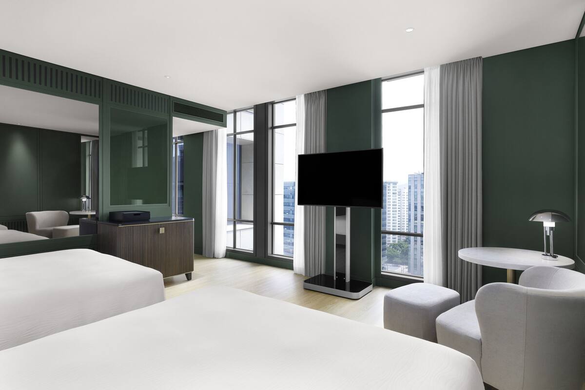 A modern hotel room with a large bed, a desk, a flat-screen TV, and a view of the city.