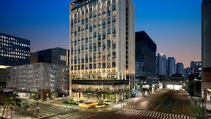A modern hotel with a grid of windows, a prominent 'GRAVITY' sign, and a well-lit entrance area with a crosswalk. - GRAVITY JOSUN Seoul Pangyo, Autograph Collection (Seongnam)