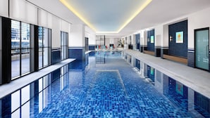 A modern hotel lobby with a long reception desk, a pool area with blue-tiled flooring, and large windows offering views of the city. - GRAVITY JOSUN Seoul Pangyo, Autograph Collection (Seongnam)