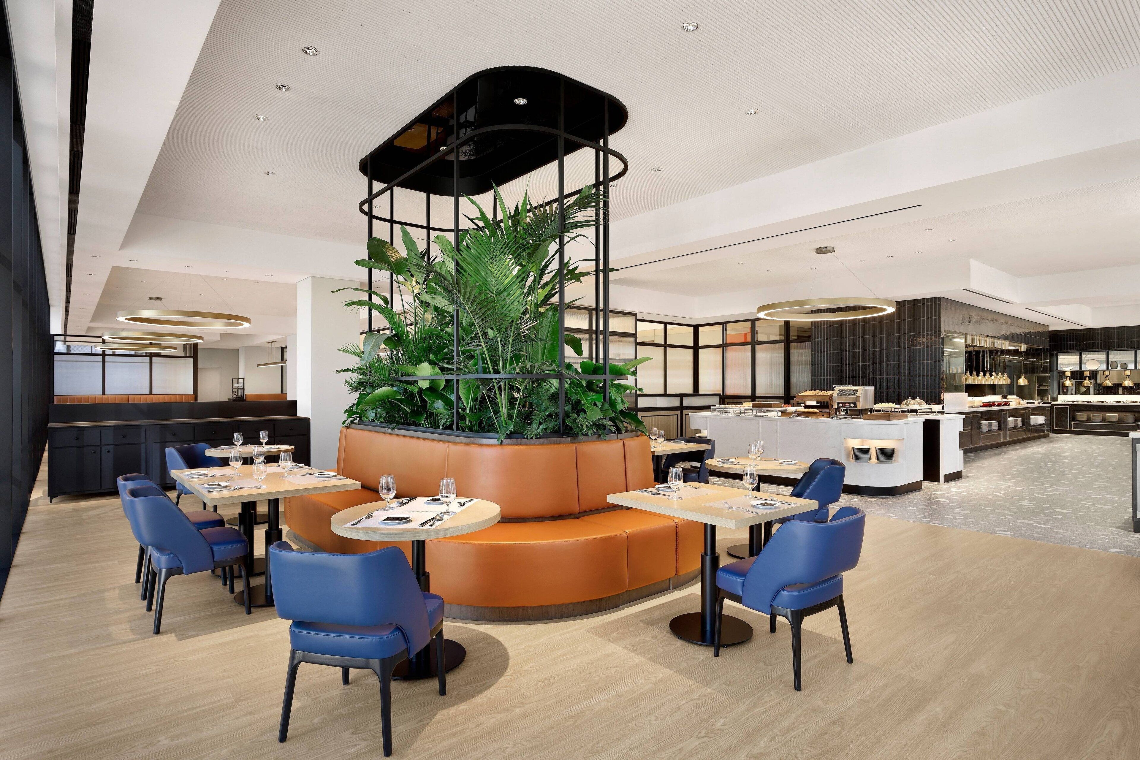 Een modern restaurant met een centraal zitgedeelte, bestaande uit een cirkelvormige opstelling van tafels en stoelen, omgeven door een groene strook en een zwarte decoratieve constructie.