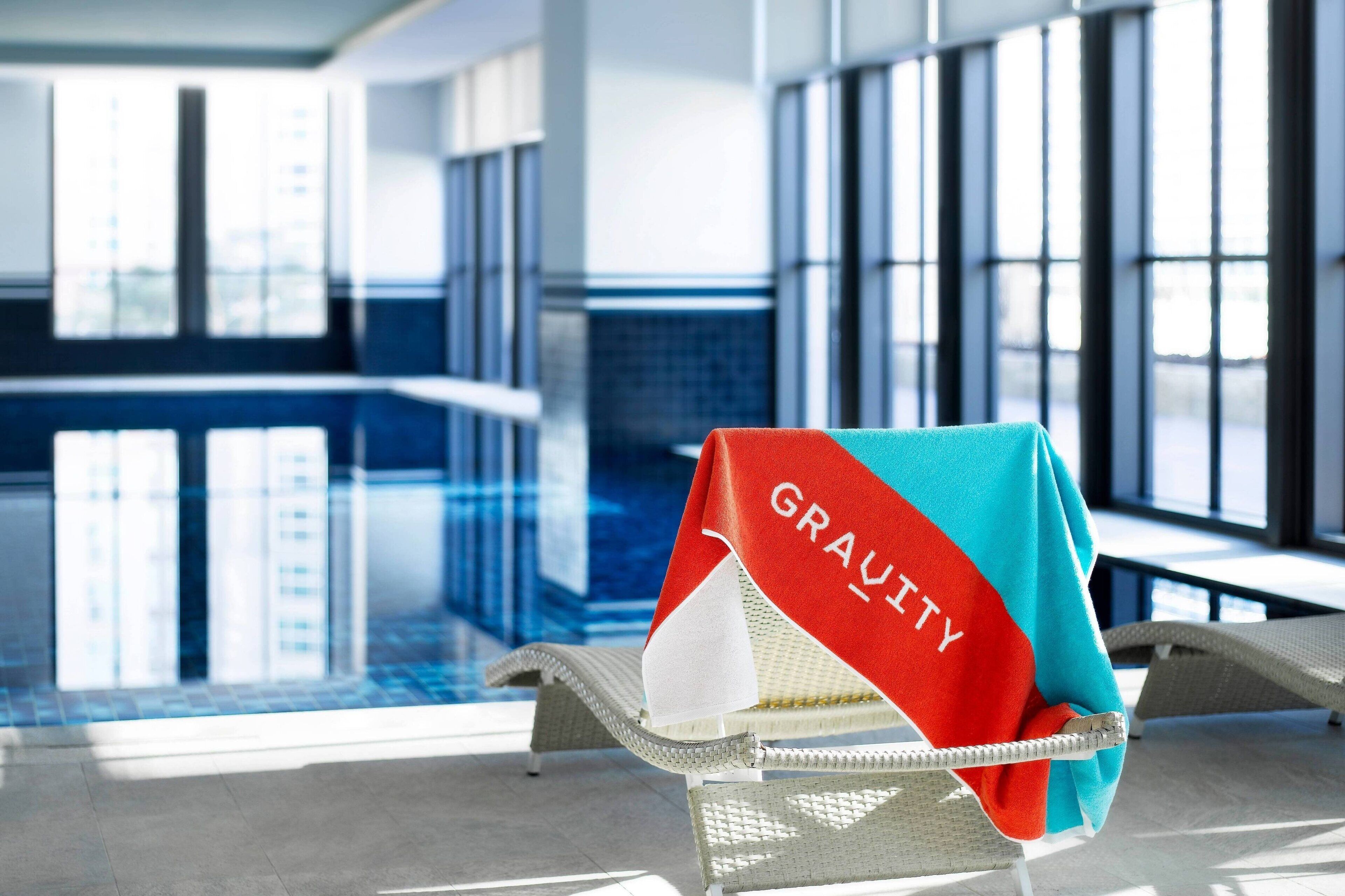 A lounge chair with a towel draped over it, a pool, and a view of a building with large windows.