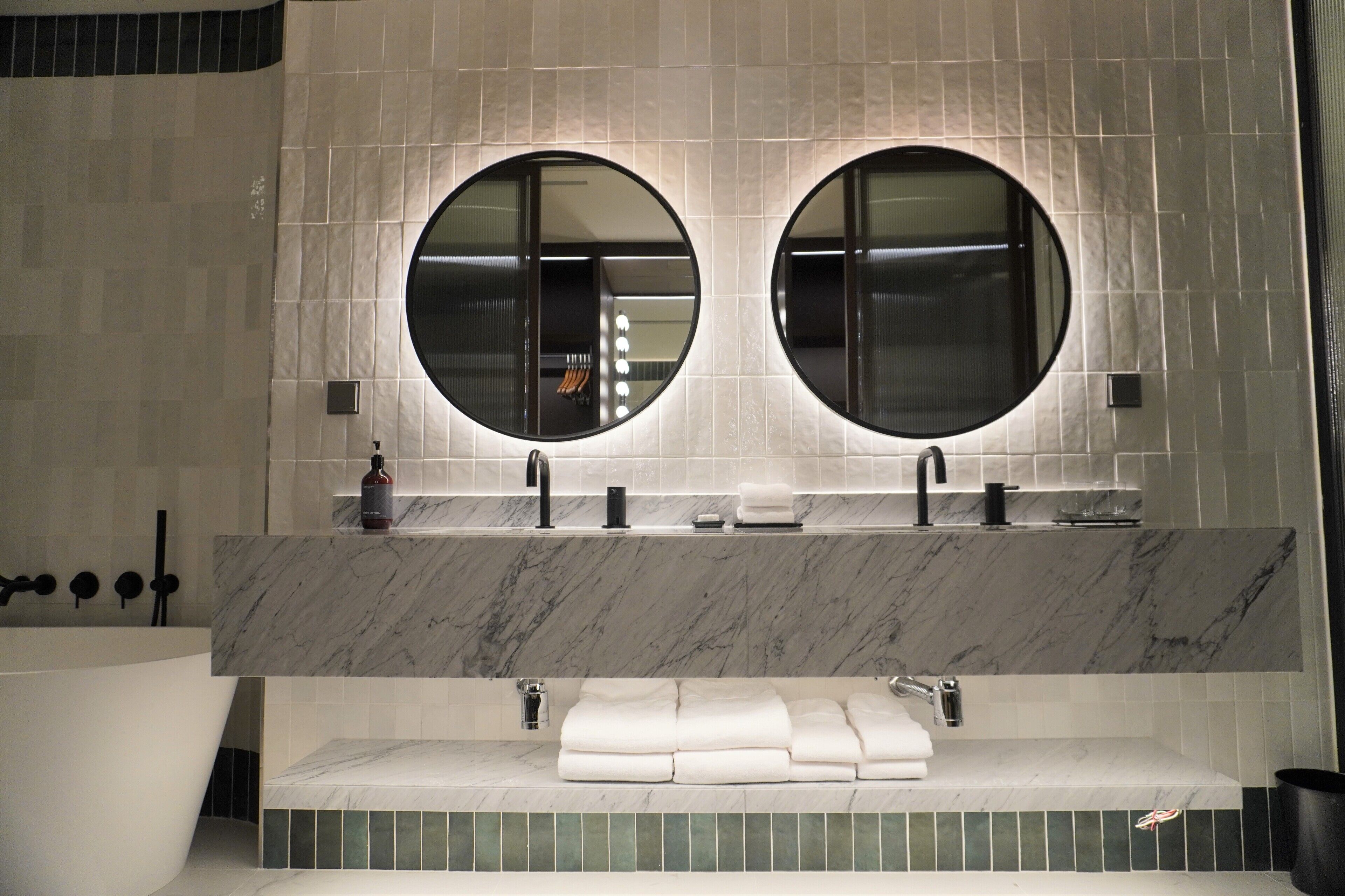 A modern bathroom with two round mirrors, a large bathtub, and a marble countertop.