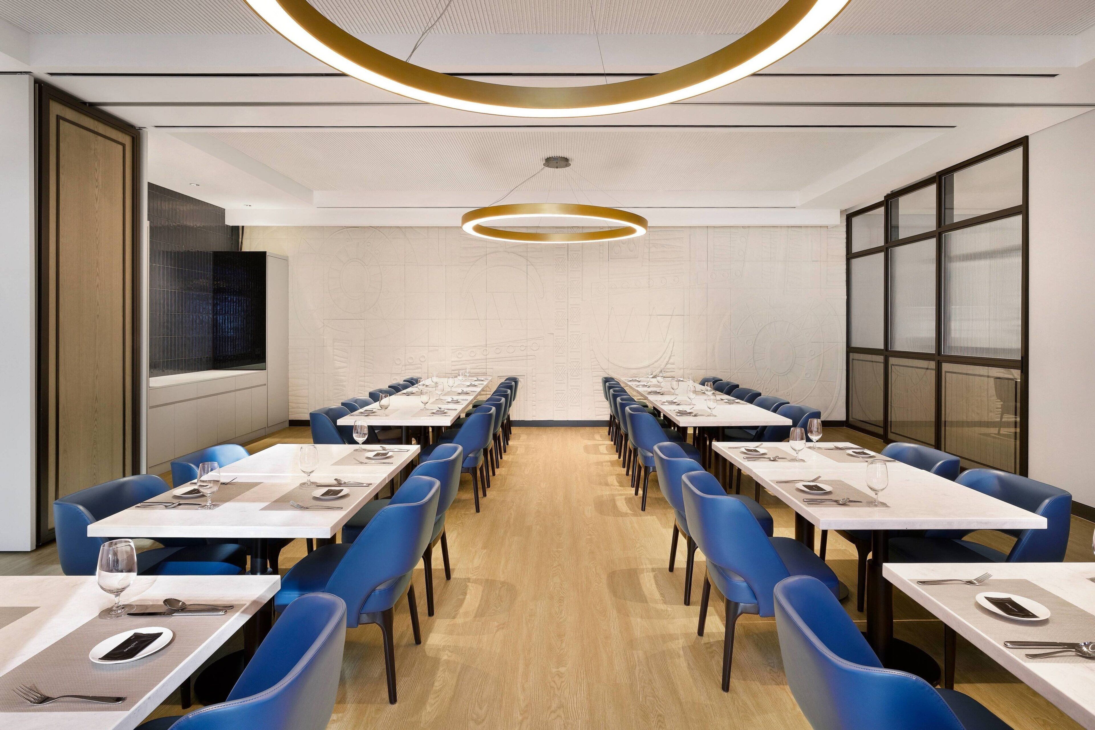 Een vergaderzaal met lange tafels, blauwe stoelen en een modern plafondontwerp.