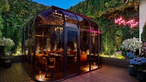 A glass-enclosed dining area with a wooden deck, surrounded by lush greenery and a neon sign. - GRAVITY JOSUN Seoul Pangyo, Autograph Collection (Seongnam)