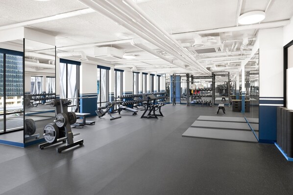 A modern gym with various exercise equipment, large windows, and a clean, organized layout.