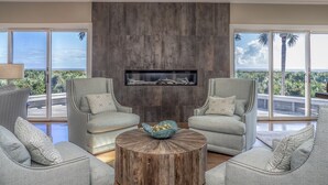 A living room with two grey armchairs, a round wooden coffee table, and a built-in fireplace. - Incredible Oceanfront Home-Sleeps 8! Huge Deck! Beach Access! Amenity access included (Seabrook Island)