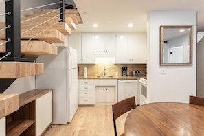 Una cocina moderna con armarios blancos, una escalera de madera, una mesa de comedor y un horno empotrado.
