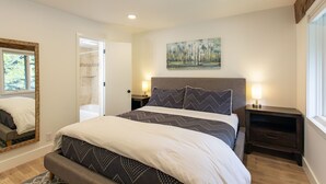 A bedroom with a bed, bedside tables, a nightstand, a painting, and a window.