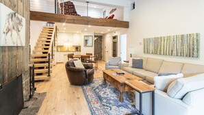A spacious living area with a high ceiling, a wooden staircase, a sofa, a coffee table, and a rug.