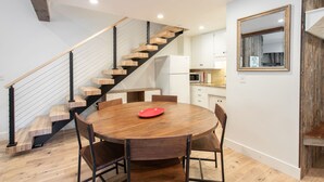 A modern kitchen with white cabinets, a wooden staircase, and a round dining table with chairs.