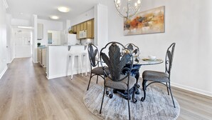 Una cocina moderna con armarios blancos, una isla central y un comedor con una mesa redonda y sillas de metal.