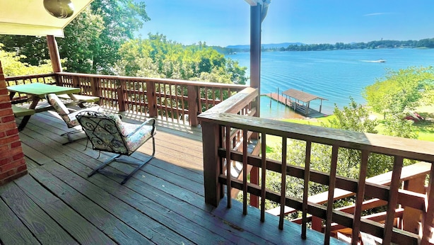 Eine Holzterrasse mit Gartenmöbeln, Blick auf einen See und einem Steg.