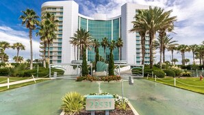 Un hotel moderno con fachada curva, palmeras y una escultura central.