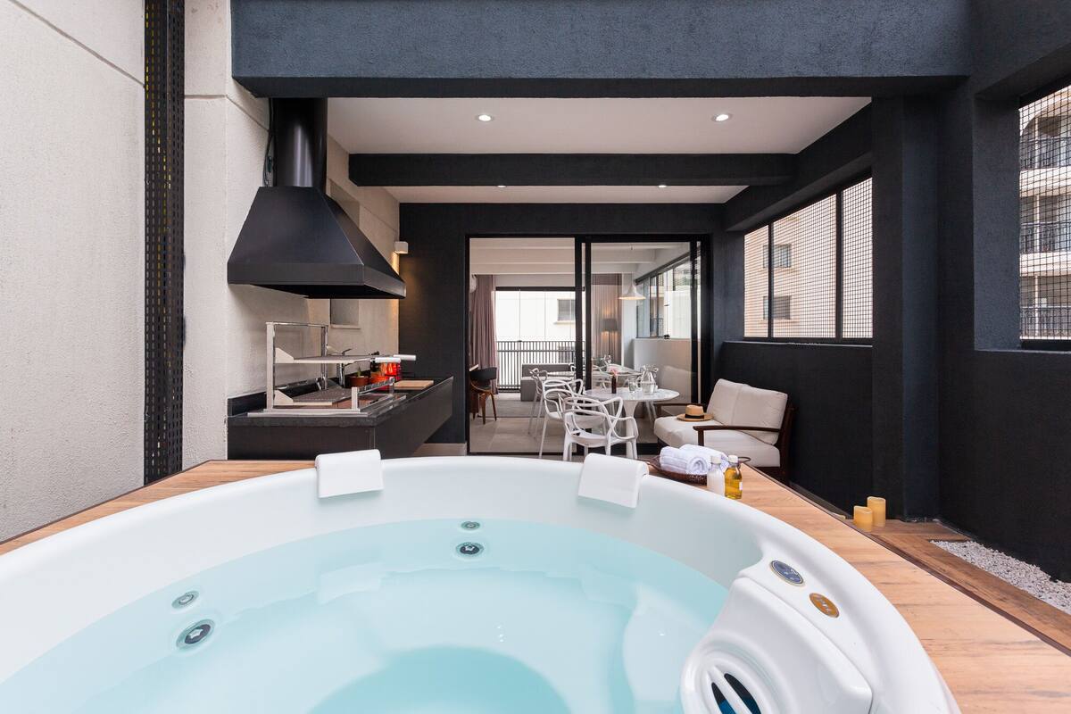 Un área interior de piscina moderna con un jacuzzi, asientos y vistas al balcón exterior.