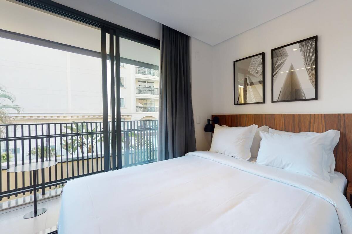 Habitación de hotel con una cama grande, cabecera de madera, vista a un balcón y dos cuadros enmarcados en la pared.
