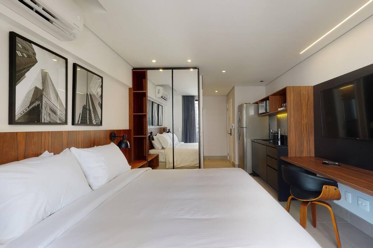 Una habitación de hotel moderna con una cama grande, un escritorio con una silla, un televisor y una kitchenette.