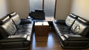 A living room with two black leather sofas, a wooden coffee table, and a sliding glass door leading to a balcony.