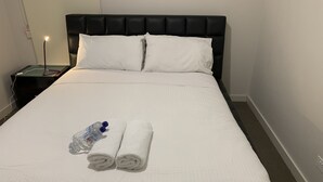 A neatly made bed with white linens, a water bottle, and two rolled towels on the bed.