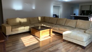 A living room with a sectional sofa, a wooden coffee table, and hardwood flooring.