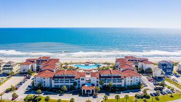 A hotel with multiple buildings, a central pool, and a beach view.