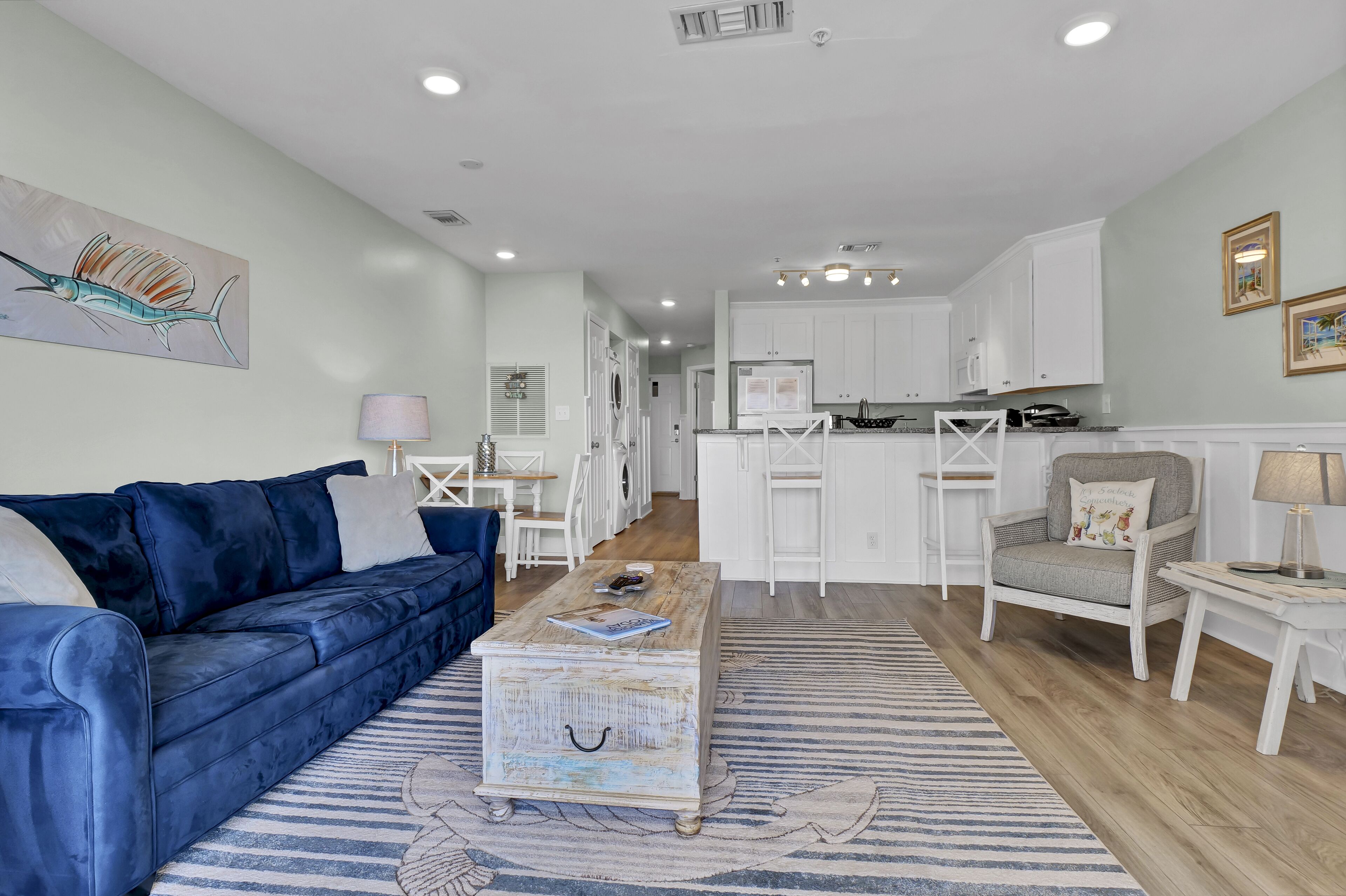 A modern living room with a blue sofa, a coffee table, and a kitchen in the background.