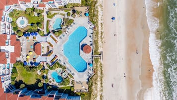 An aerial view of a resort with multiple swimming pools, beach access, and a variety of outdoor seating areas.