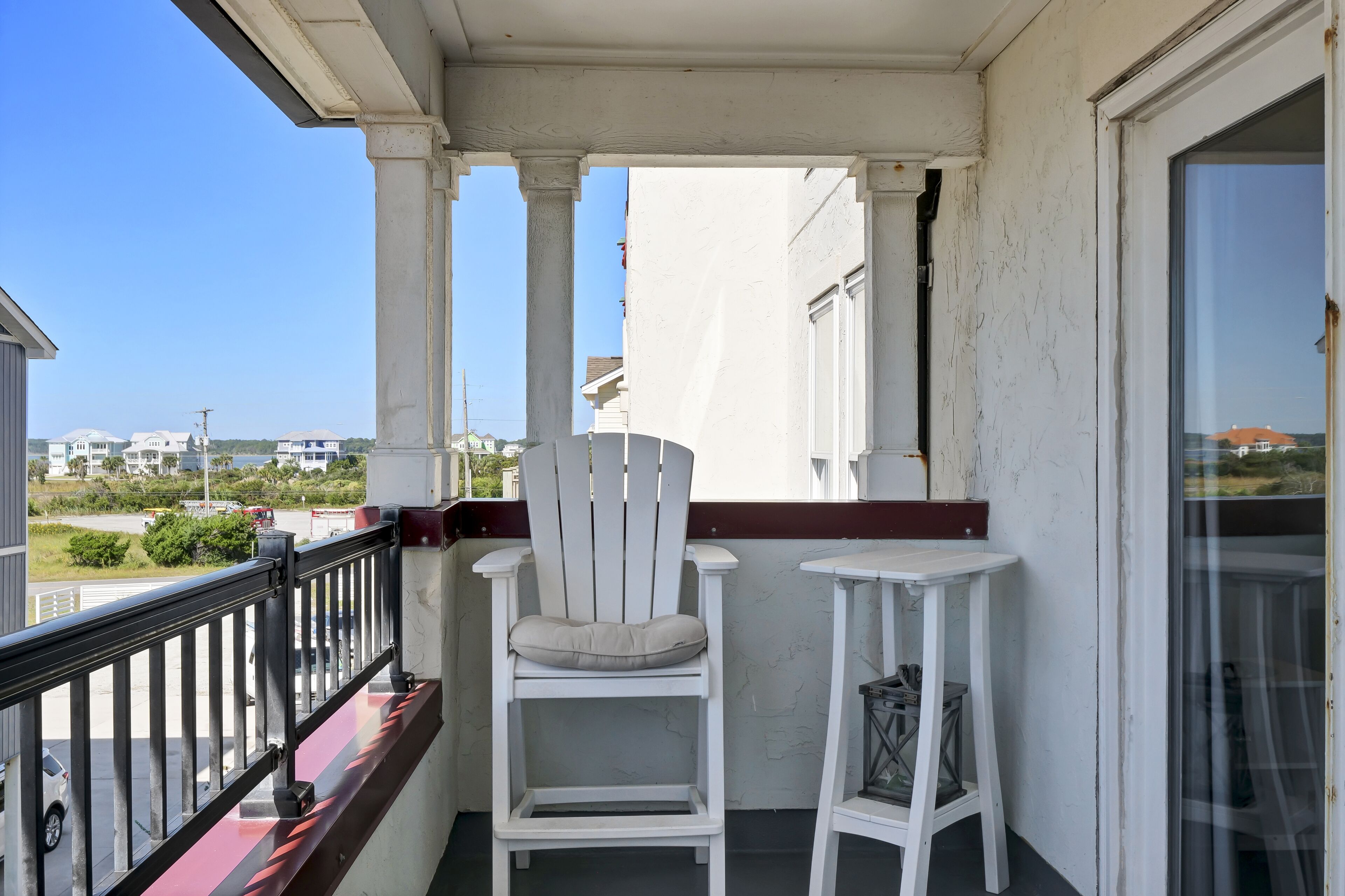 A balcony with a white chair and a small table, overlooking a residential area.