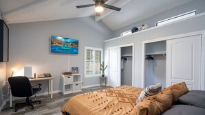 Une chambre à coucher comprenant un lit, un bureau, une chaise, un ventilateur de plafond et un téléviseur.