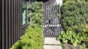Un bâtiment moderne à la façade sombre, avec un étroit chemin et une clôture en bois.