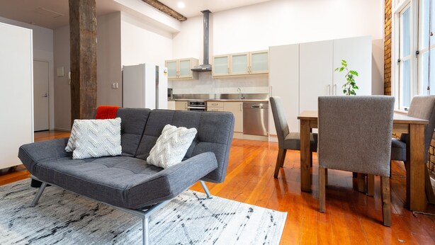A modern living room with a grey sofa, a dining table with chairs, and a kitchen in the background. - Toodle's Characterful loft on Lorne Street (Auckland)