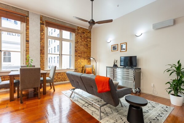 A modern living room with a sofa, dining table, and chairs, a ceiling fan, a TV, and a potted plant. - Toodle's Characterful loft on Lorne Street (Auckland)