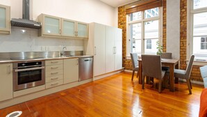 A modern kitchen with stainless steel appliances, white cabinetry, and a dining area with a brick accent wall and large windows. - Toodle's Characterful loft on Lorne Street (Auckland)