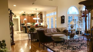 A spacious living room with a wooden floor, a sofa, a coffee table, and a dining area with chairs and a table. - Gorgeous, Wooded 3 Acre Estate -5 Bed/4  Bath-Leesburg/Brambleton/Aldie area (Leesburg)