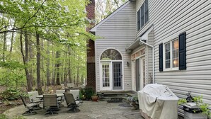 A stone patio with outdoor furniture, a covered grill, and a house with a brick chimney. - Gorgeous, Wooded 3 Acre Estate -5 Bed/4  Bath-Leesburg/Brambleton/Aldie area (Leesburg)