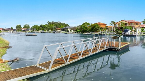 A wooden dock extending over calm water, surrounded by residential buildings and greenery. - Nabilla Court - Waterfront Luxury with Shared Pontoon & Paddleboards - Holiday Yamba (YAMBA)