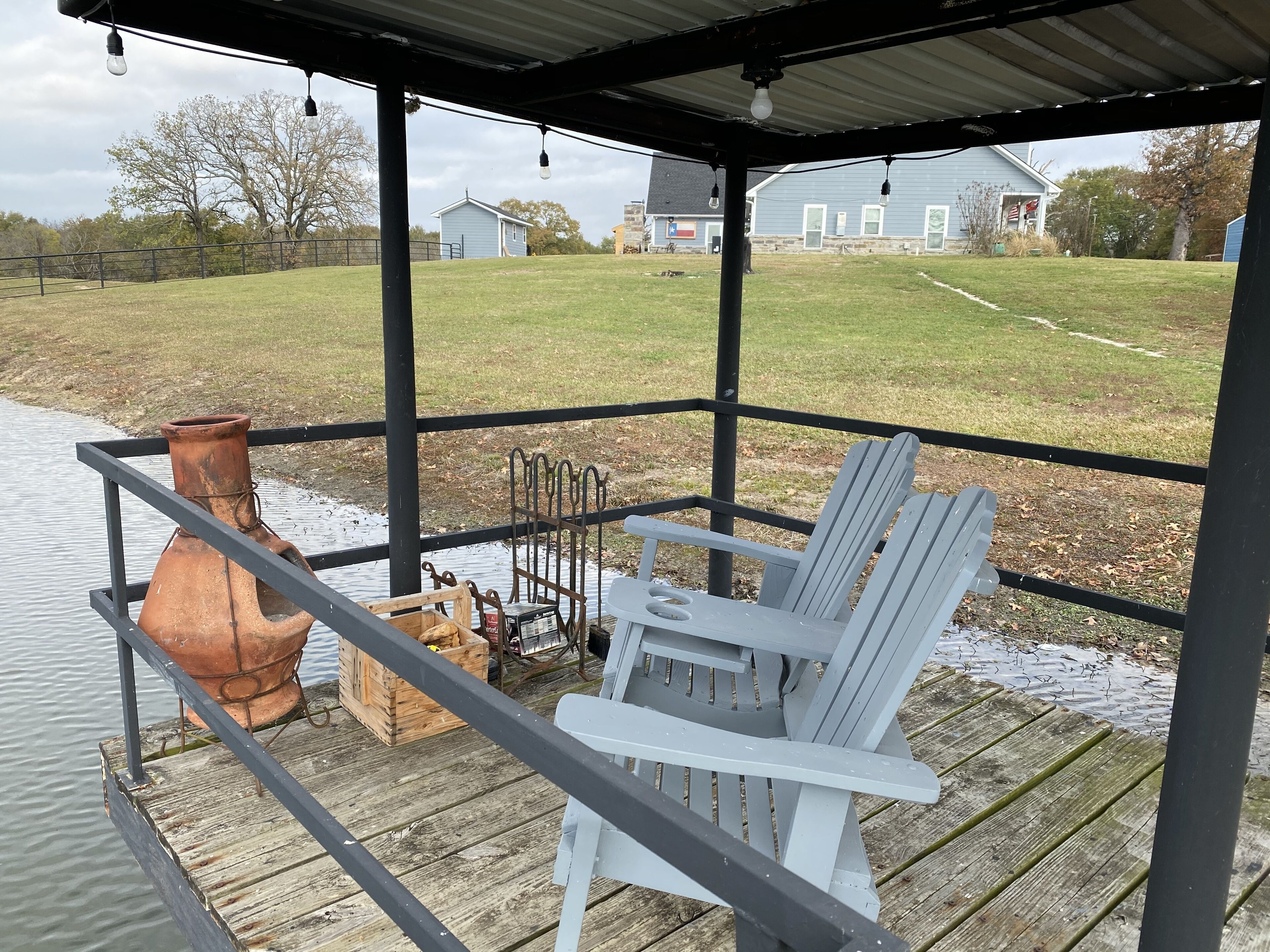 Un espace extérieur abrité doté d’une terrasse en bois, d’une chaise Adirondack blanche, d’un pot en terre cuite et d’une étagère en métal.