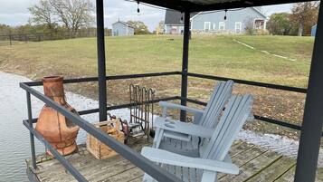 Un espace extérieur abrité doté d’une terrasse en bois, d’une chaise Adirondack blanche, d’un pot en terre cuite et d’une étagère en métal.