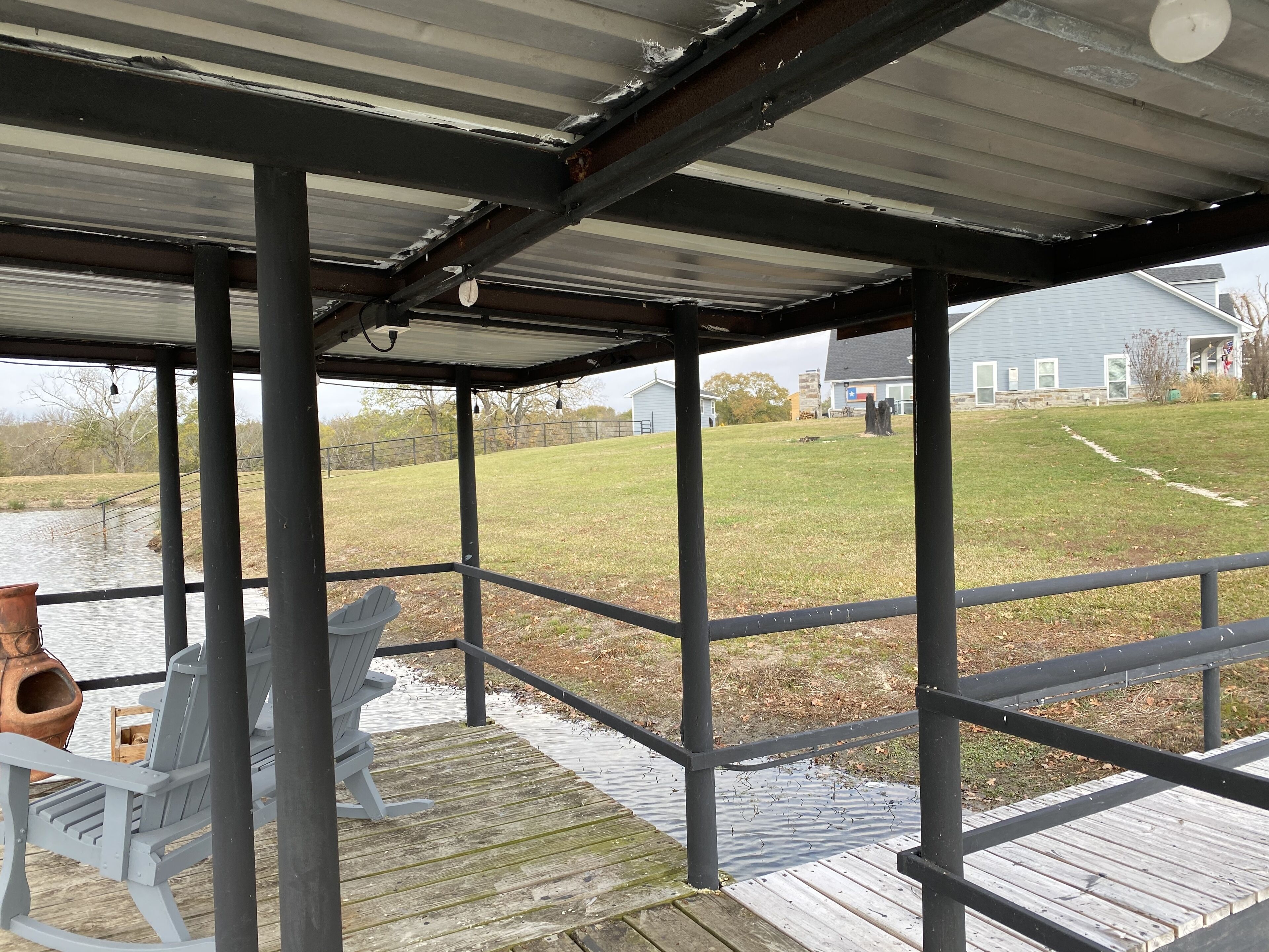 Um espaço ao ar livre coberto com um deck de madeira, duas cadeiras Adirondack, e vista para um gramado e uma casa ao fundo.