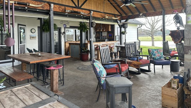 An outdoor patio area with wooden tables and chairs, a bar, and a view of a lake. - Double D Ranch Guest House (Emory)