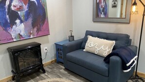 A living room with a blue sofa, a black entertainment unit, a large abstract painting, a woven rug, and a floor lamp. - Double D Ranch Guest House (Emory)